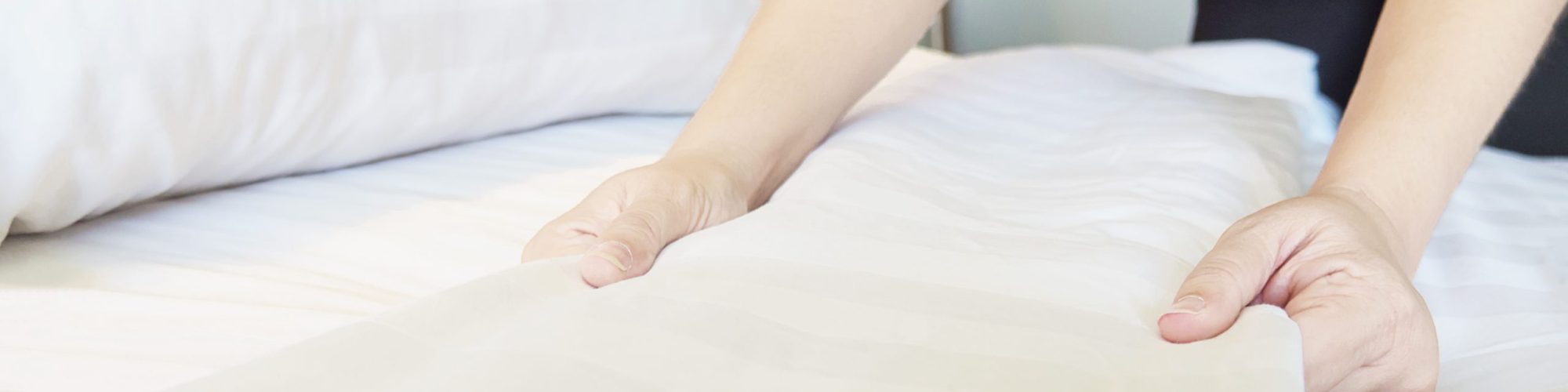 Lady hands set up white bed sheet in hotel room